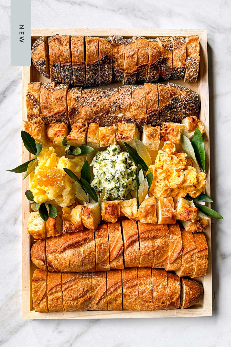 Assorted baguettes and artisanal breads on a board with three handmade artisanal butters from Vermont.