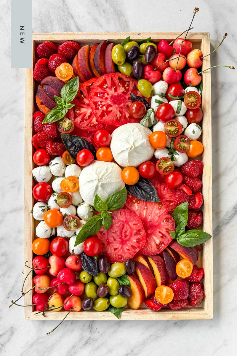 Assorted fresh heirloom tomatoes and fruits, with Burrata and mozzarella  cheese in a wooden tray on a marble surface
