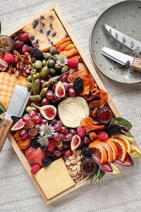 A set of 3 rustic acacia wood cheese knives on a speckled pottery plate next to a cheese board.