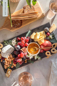 A slate cheese board filled with cheese, fruits, nuts, and jam lit by late afternoon sunlight.