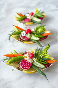 A trio of fresh vegetable single serve crudite grazing boats, filled with the season's freshest vegetables paired with a scoop of lemon dill hummus, accented with fresh flowers and herbs.