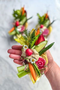 A trio of fresh vegetable single serve crudite grazing boats, filled with the season's freshest vegetables paired with a scoop of lemon dill hummus, accented with fresh flowers and herbs.