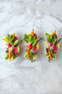 A trio of fresh vegetable single serve crudite grazing boats, filled with the season's freshest vegetables paired with a scoop of lemon dill hummus, accented with fresh flowers and herbs.