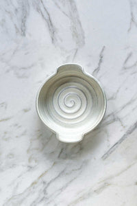 A handmade stoneware brie baker with a creamy, off-white glaze sitting on a marble countertop.