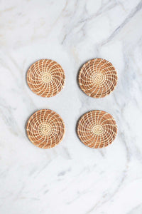 A set of four handmade longleaf pine needle coasters on a white marble counter.
