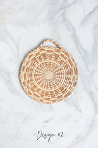 A close up picture of a handmade longleaf pine needle trivet in Design #2 on a white marble background.
