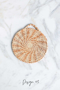 A close up picture of a handmade longleaf pine needle trivet in Design #3 on a white marble background.
