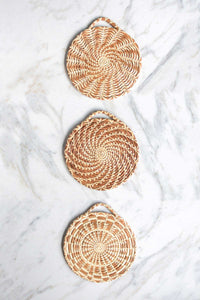 Three handmade longleaf pine needle trivets in three different patterns on a white marble counter.