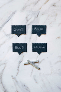 A box set of natural slate cheese markers with soapstone chalk to write the type of cheese on the cheese board.