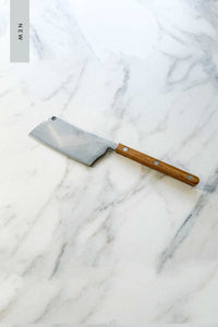 The NEW Bistrot Cheese Cleaver, In Vintage Teak lying on a marble counter.