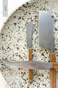 The NEW Bistrot Cheese Knives Set, In Vintage Teak lying on handmade speckled pottery plate.