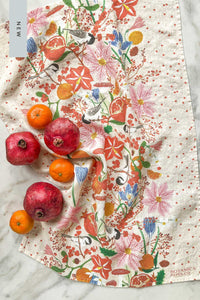 A wintry linen tea towel with pomegranates, chickadees, clementines, amaryllis, and poinsettia flowers.