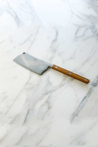 The Bistrot Cheese Cleaver, In Vintage Teak lying on a marble counter.