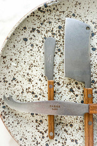 The Bistrot Cheese Knives Set, In Vintage Teak lying on handmade speckled pottery plate.