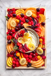 A ready-to-eat seasonal fruit platter featuring fresh melons, stone fruit, berries, kiwi, and edible flowers on a marble counter, available for Vermont delivery.