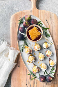 An oval stoneware serving tray filled with fresh figs topped with ricotta drizzled with honey.