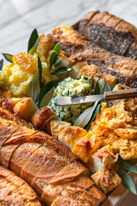 Assorted baguettes and artisanal breads on a board with three handmade artisanal butters from Vermont.