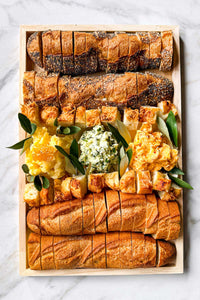 Assorted baguettes and artisanal breads on a board with three handmade artisanal butters from Vermont.