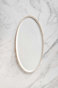 A white ceramic oval serving platter on a marble counter.