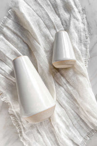 A pair of white stoneware bud vases with raw clay edges and bases, lying on an ivory linen napkin.