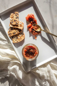 A white porcelain platter with an open jar of Cherry Sherry Fennel Honey Jam with a spoonful smeared on the tray next to crackers.