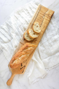 A Spalted Maple baguette board on a linen cloth with sliced baguette on it.