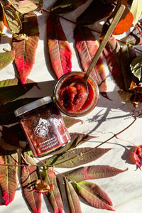 Fall colored leaves and vines are a backdrop for jars of Strawberry Italian Plum Rosewater Honey Jam.