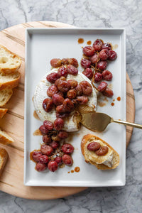 A white platter with Baked Brie With Roasted Grapes on top of a large round wooden board.